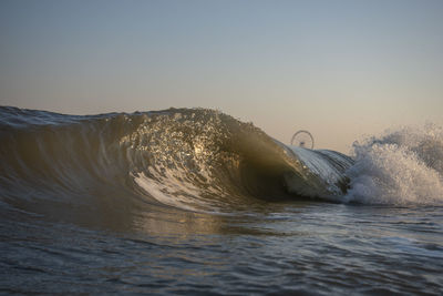 Waves splashing in sea against clear sky during sunset