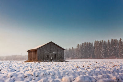 Cottage on snow covered landscape against clear sky