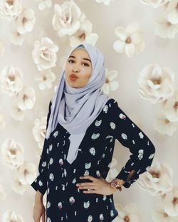 Portrait of smiling woman wearing hijab standing against floral patterned wall