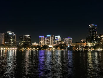 Illuminated buildings by river against clear sky at night