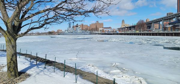 Frozen river by buildings in city against sky