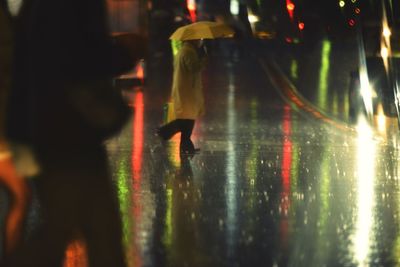 People with umbrella walking on illuminated wet street at night during monsoon