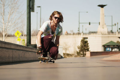 Man in sunglasses skateboarding on footpath