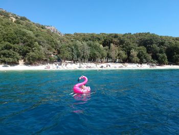 Boy floating on water against clear blue sky