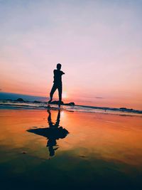 Silhouette man standing on shore at beach against sky during sunset