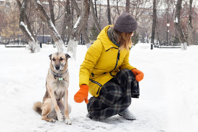 Young woman is walking with her dog in a snowy winter park.