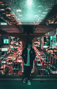 Full length of man wearing mask standing on footbridge over highway