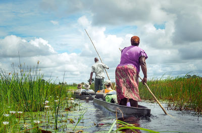 Rear view of people sailing in lake against sky