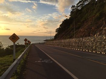 Road by sea against sky during sunset