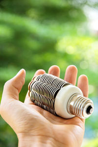 Cropped hand of man holding light bulb against plants