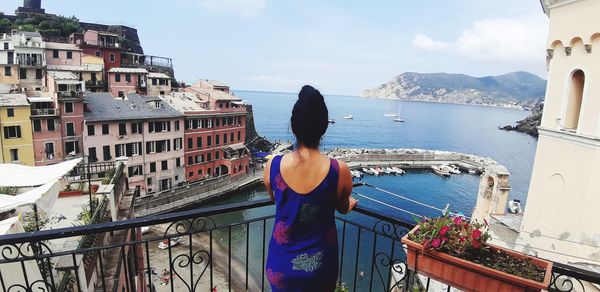 Rear view of woman looking at sea by buildings against sky