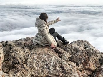 Rear view of woman sitting on rock against sky