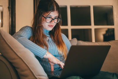 Young woman using laptop while sitting on sofa at home