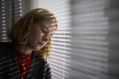 Pensive teenage girl looking through window