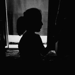 Side view of silhouette woman looking through window at home