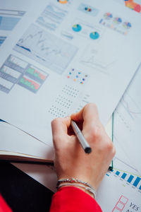 Cropped hand of businesswoman writing in book at office