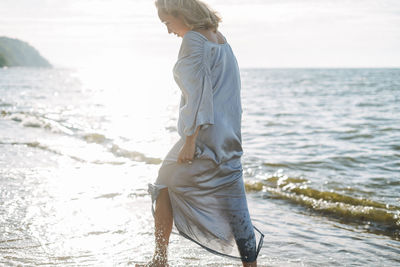 Young woman with long hair in silk blue dress enjoying life on sea beach