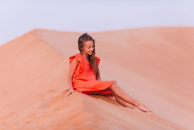 Portrait of young woman on sand in desert against sky