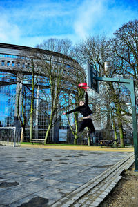 Man jumping by plants in city against sky