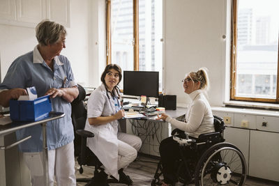 Female healthcare worker sitting with disabled patient talking with senior nurse working in medical clinic