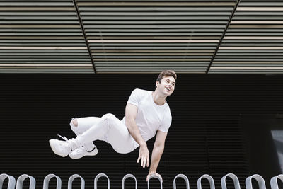 Young man looking away while jumping over railing