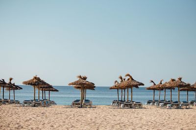 Lounge chairs and parasols on beach against clear sky