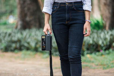 Midsection of woman holding camera while standing on land