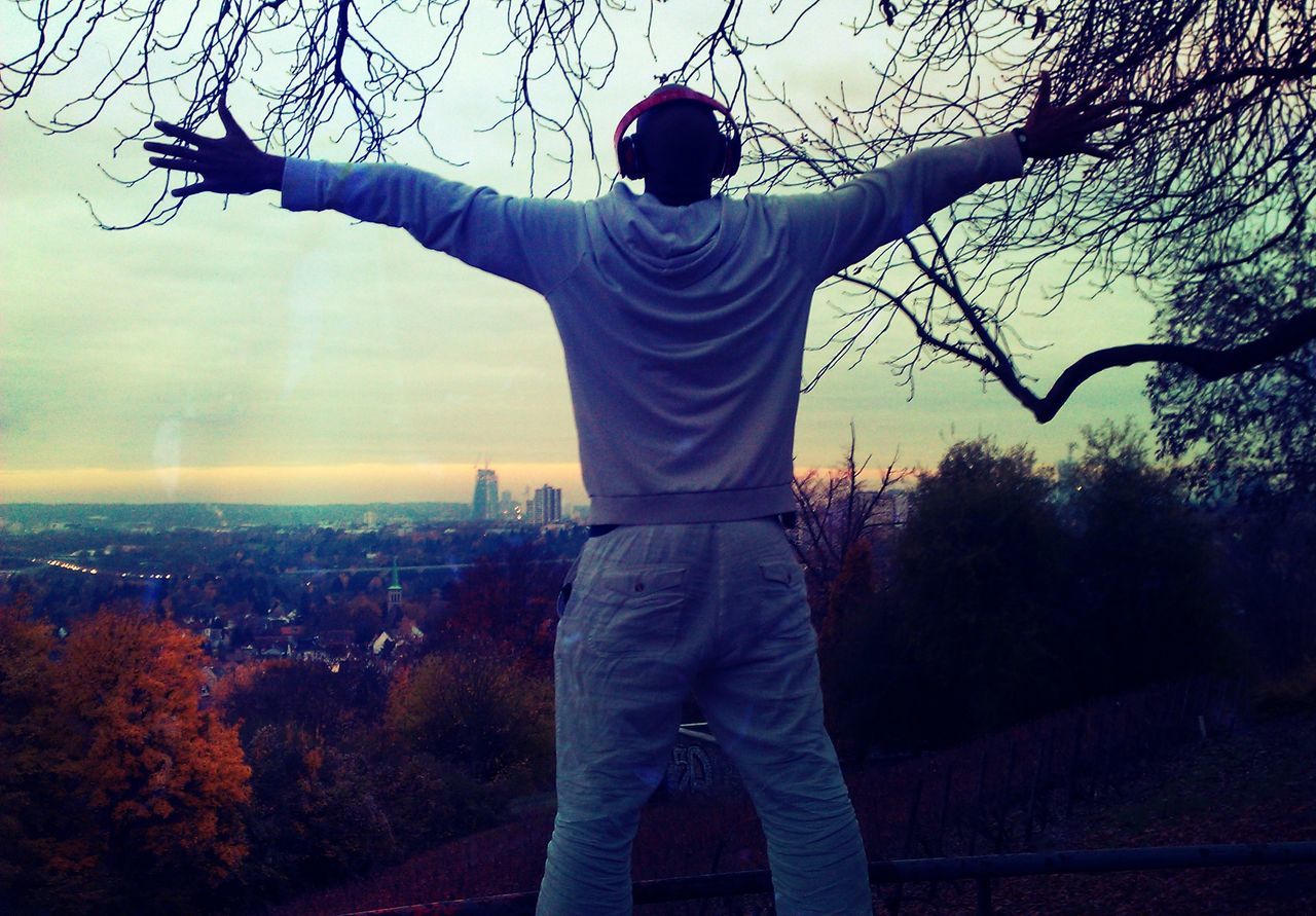 standing, lifestyles, tree, casual clothing, leisure activity, full length, three quarter length, sky, rear view, arms outstretched, young adult, person, bare tree, young men, nature, silhouette, front view, sunset