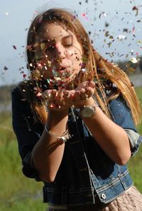 Young woman blowing confetti while standing on field