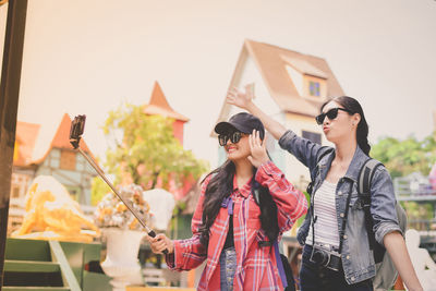 Happy friends taking selfie while standing against houses