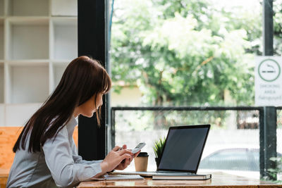 Woman using phone while sitting on table