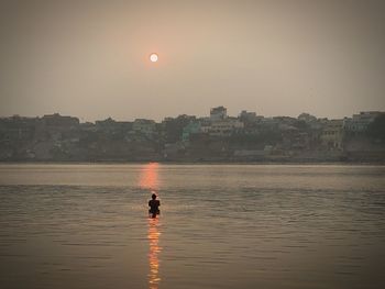 Silhouette of woman on river against sunset sky