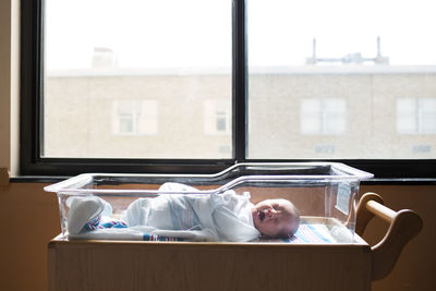 Baby boy yawning while sleeping in crib by window at hospital