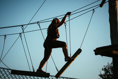 Low angle view of girl walking on rope against sky