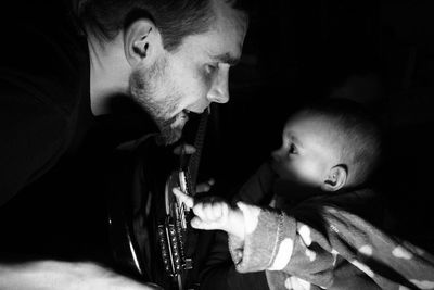 Father with guitar looking at baby against black background