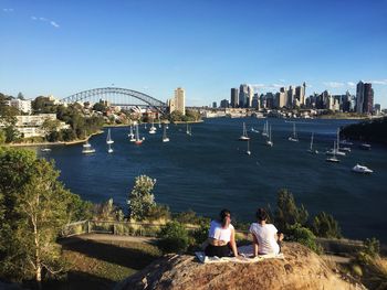 Rear view of women sitting on rock at balls head reserve against sydney harbor in city