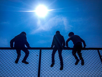 Low angle view of silhouette people sitting on chainlink fence