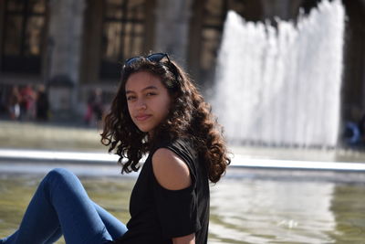 Portrait of teenage girl sitting against fountain