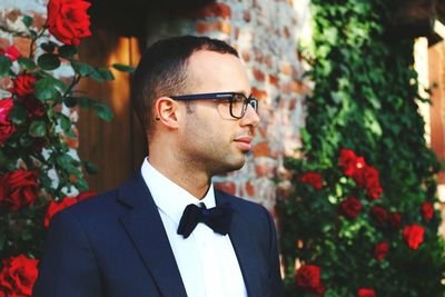 Young man wearing suit standing by rose plants outside house