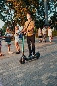 Full length of young man wearing flu mask standing on electric push scooter