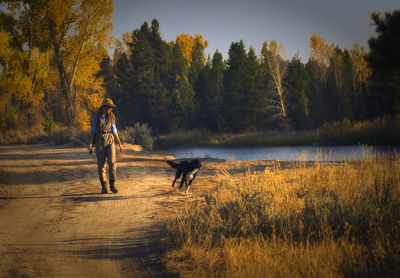 Full length of woman with dog walking on land in forest