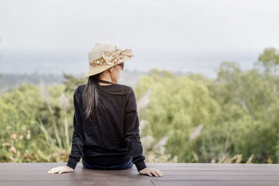 Rear view of woman sitting against trees on wood