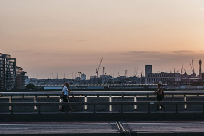 People on bridge against sky during sunset