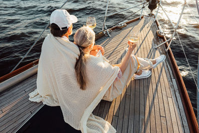 Rear view of couple sitting on boat sailing in sea