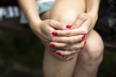 Red nail polish. girl closed her fingers. hands on knee. posture details. long fingers. 