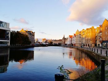 River amidst buildings in city against sky at sunset