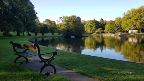 Bench in park by lake against sky