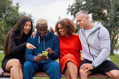 Smiling friends looking at phone sitting on bench at park