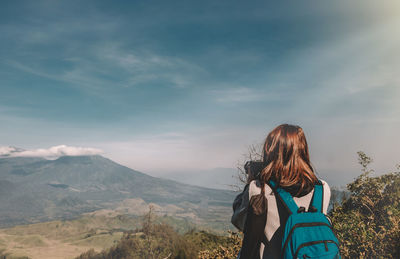 Rear view of woman with backpack photographing mountains while standing against sky