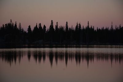 Sunset colors and alpenglow reflected in high elevation lake with wind ripples and forest 